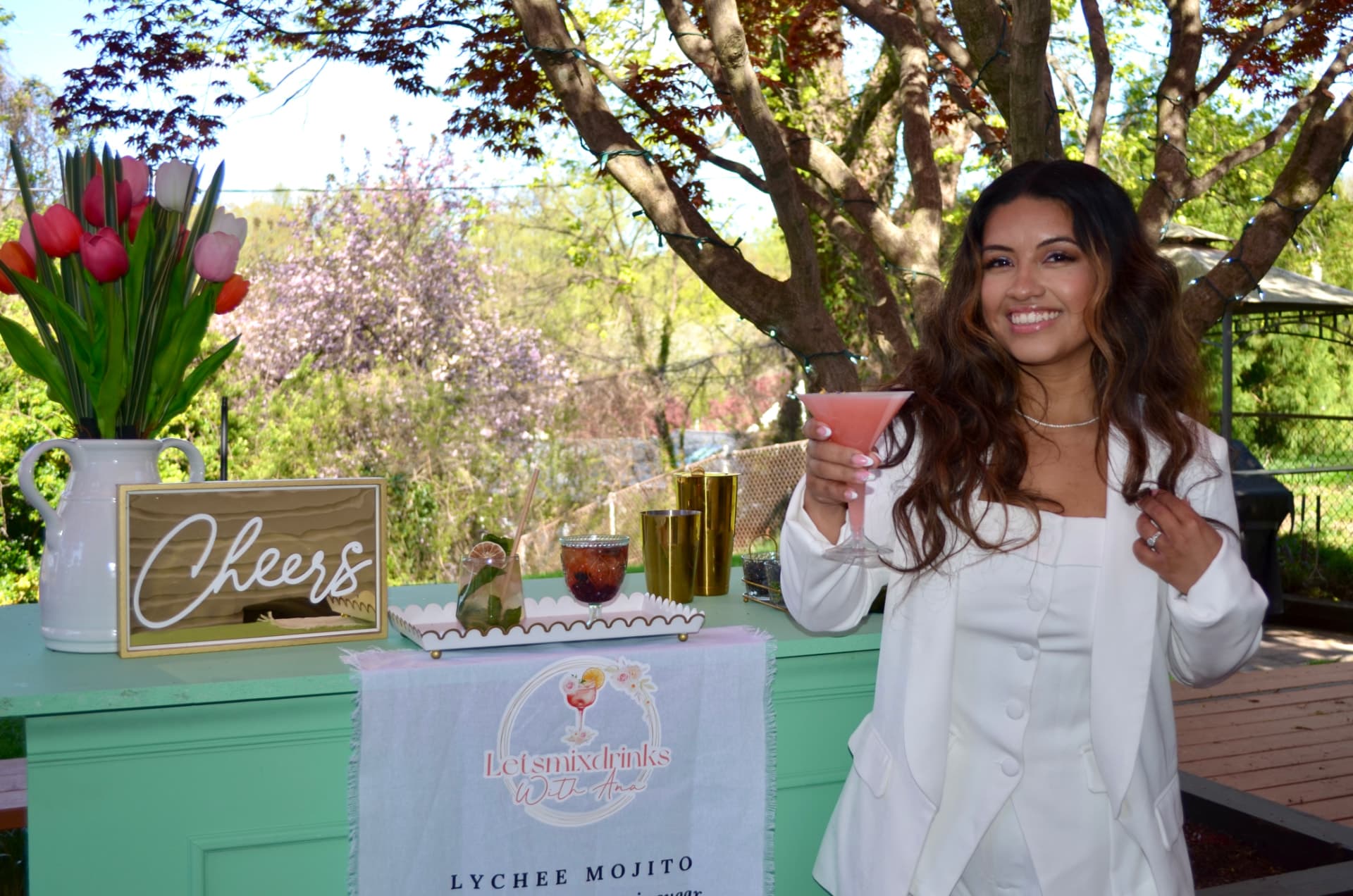 Ana smiling behind a mint mobile bar with a pink cocktail and a Cheers sign