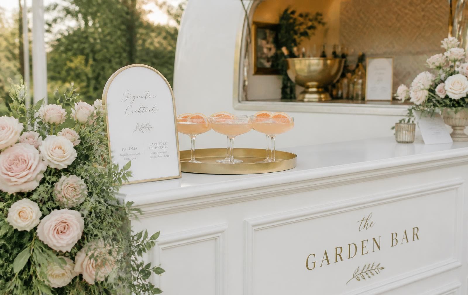 Luxury white wedding bar styled with blush roses and a tray of signature cocktails